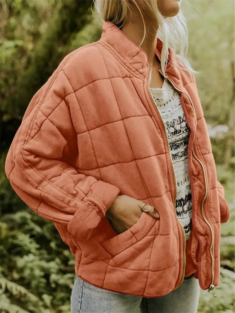 Frau in orangefarbener Steppjacke, lässig offen getragen, mit gemustertem Pullover darunter. Modetrend Herbst, Outdoor-Bekleidung, Damenmode.