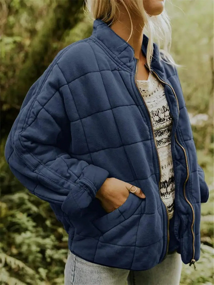 Frau in blauer Steppjacke im Freien, trägt gestreiftes Oberteil und Jeans. Modetrend Herbst, Outdoor-Bekleidung, warme Jacke.