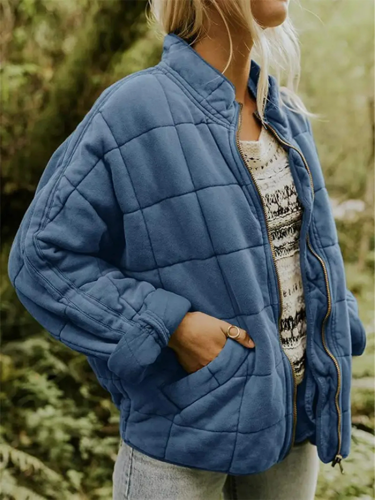 Frau in blauer Steppjacke im Freien, trägt gestreiftes Oberteil und Jeans. Modetrend Herbst, Outdoor-Bekleidung, bequeme Damenjacke.