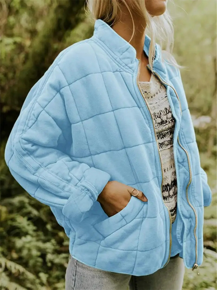 Frau in hellblauer Steppjacke, Reißverschluss offen, über gemustertem Pullover, in natürlicher Umgebung. Modetrend, Damenjacke, Outdoor-Bekleidung.