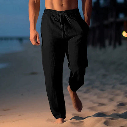 Mann in schwarzen Leinenhosen spaziert barfuß am Strand bei Sonnenuntergang. Bequeme Sommermode, Freizeitkleidung, Strandspaziergang.