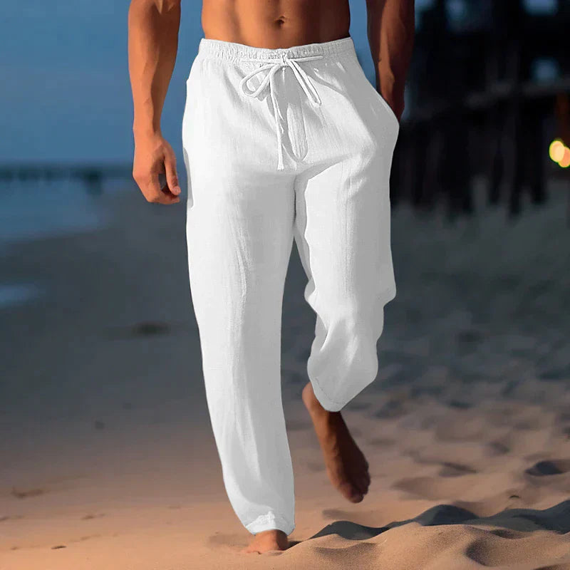 Mann in weißen Leinenhosen spaziert am Strand entlang bei Sonnenuntergang. Sommermode, Strandkleidung, Herrenbekleidung, Freizeitlook.