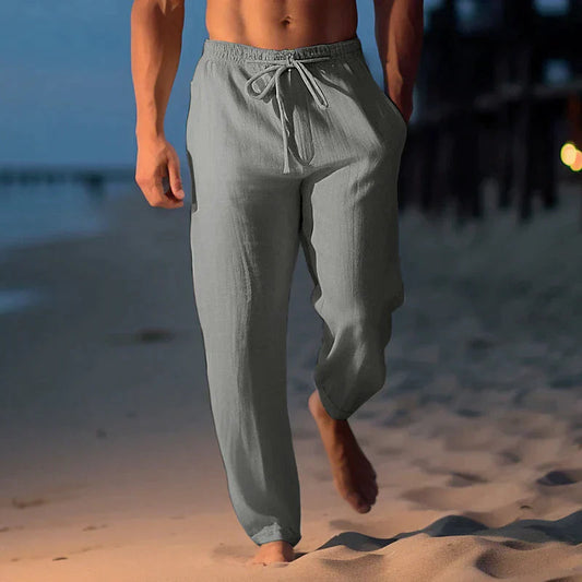Mann in grauer Leinenhose spaziert barfuß am Strand bei Sonnenuntergang. Bequeme Sommermode, Freizeitkleidung, Strandspaziergang.