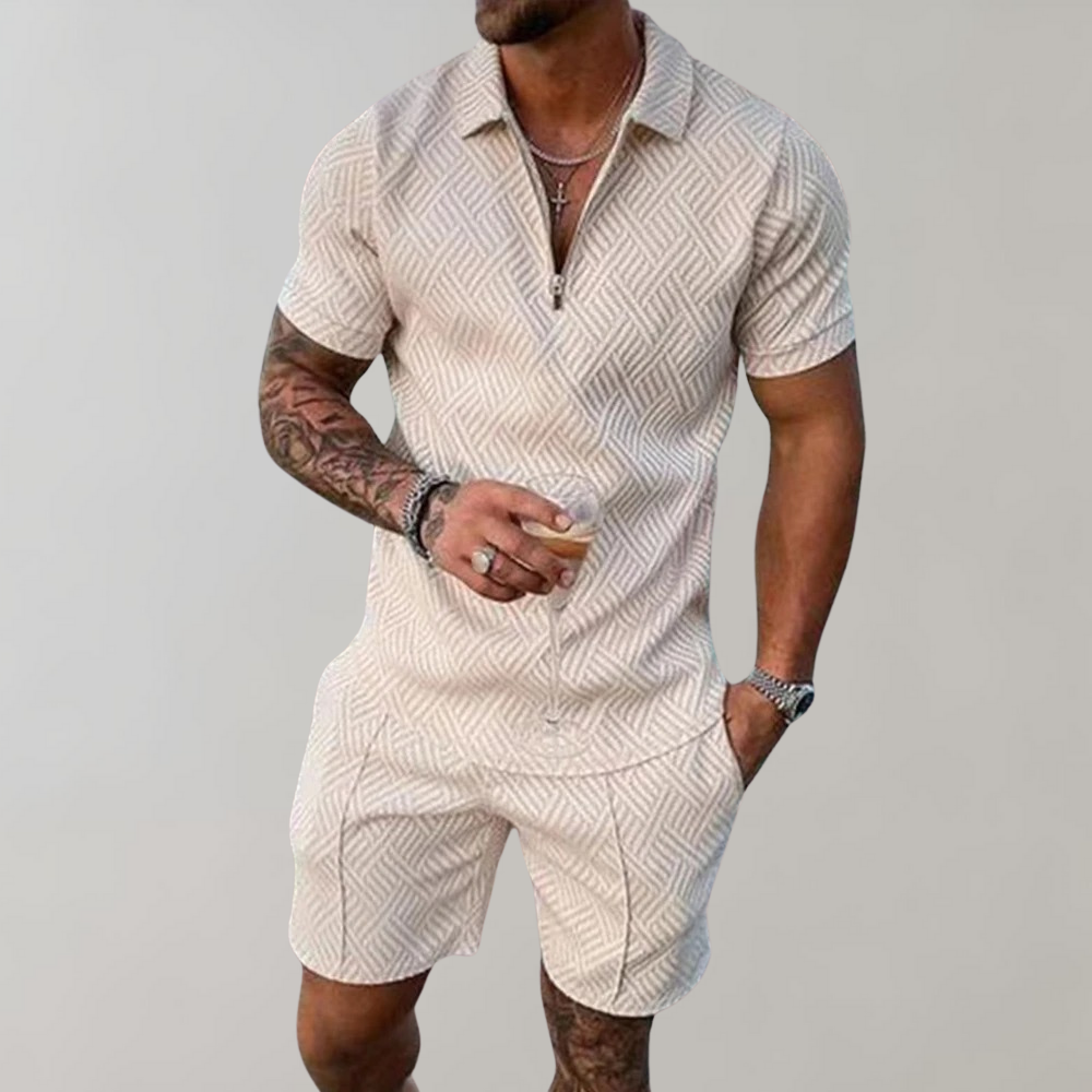 Mann in beigem, gemustertem Kurzarm-Poloshirt und Shorts, hält Getränk. Sommermode, Herrenbekleidung, lässiger Stil, tätowierter Arm.