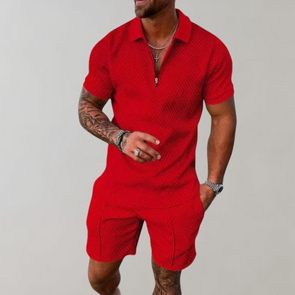 Mann in rotem, strukturiertem Kurzarm-Poloshirt und Shorts, tätowierter Arm, silberne Halskette und Armbanduhr, modischer Sommerlook.