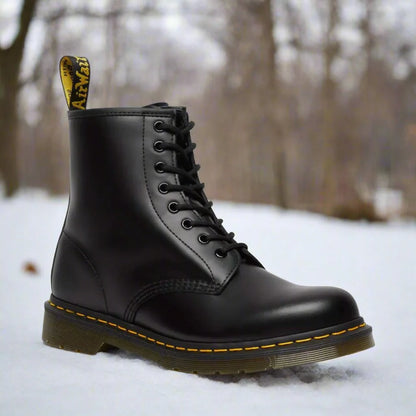 Schwarzer Lederstiefel mit gelber Naht und markantem Fersenetikett auf schneebedecktem Boden im Freien. Wintermode, robuste Stiefel, Outdoor-Bekleidung.