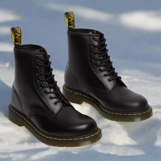 Schwarze Dr. Martens Stiefel im Schnee, ikonisches Design mit gelber Naht und Schlaufe, robuste Lederstiefel, ideal für Wintermode und Outdoor-Aktivitäten.