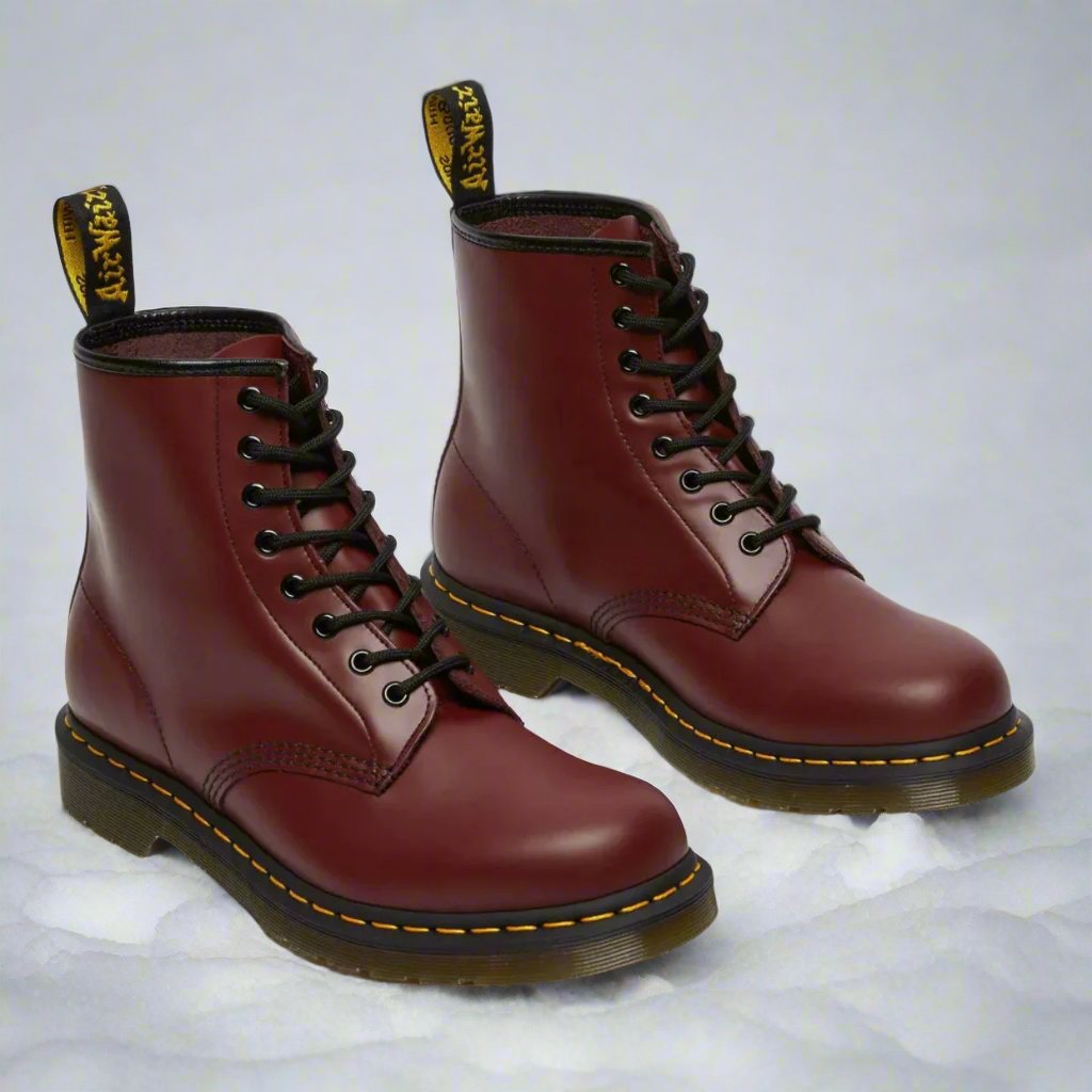 Burgunderrote Lederstiefel mit gelber Naht und schwarzer Schnürung auf weißem Hintergrund. Klassische Dr. Martens Boots, robust und stilvoll.