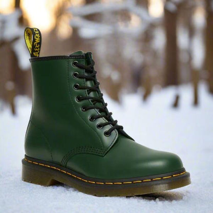 Grüner Dr. Martens Stiefel im Schnee, klassische Schnürstiefel, robustes Leder, gelbe Nähte, Wintermode, Outdoor-Boots, ikonisches Design.