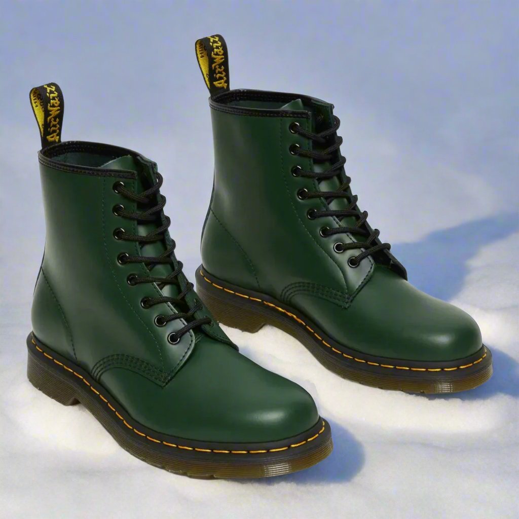 Grüne Lederstiefel auf Schnee, klassische Schnürstiefel mit gelber Naht, robuste Winterstiefel, modische Outdoor-Schuhe, Dr. Martens Stil.