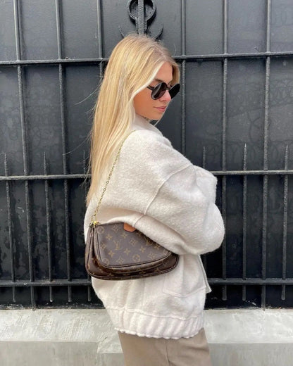 Blonde Frau mit Sonnenbrille trägt eine braune Louis Vuitton Handtasche vor einem schwarzen Gitter. Elegante Mode, Luxusaccessoire, Streetstyle.