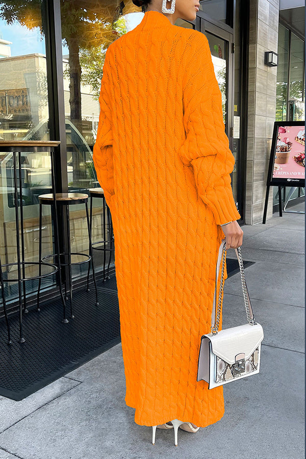 Frau in langem, orangefarbenem Strickkleid mit Zopfmuster, hält weiße Handtasche, steht vor Café. Modetrend Herbst, stilvolle Damenmode.