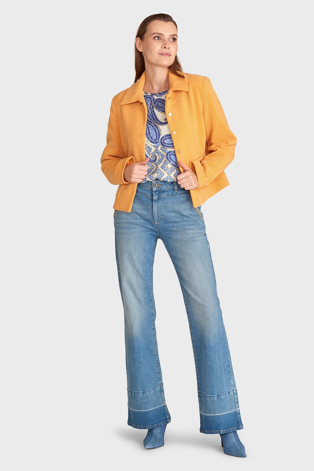 Frau in gelber Jacke, gemustertem Oberteil und blauen Schlagjeans. Modetrend Herbst, lässiger Stil, Damenmode, Freizeitlook.