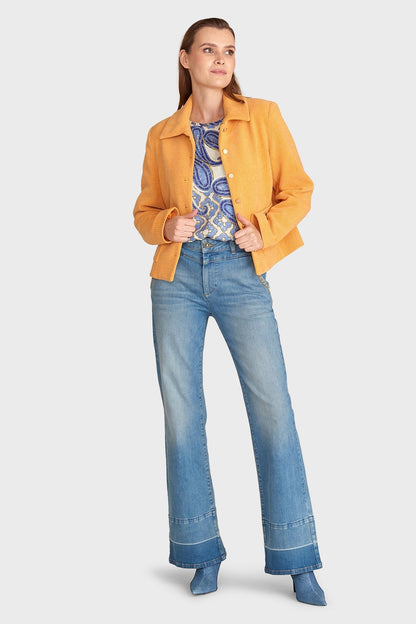 Frau in gelber Jacke, gemustertem Oberteil und blauen Schlagjeans. Modetrend Herbst, lässiger Stil, Damenmode, Freizeitlook.