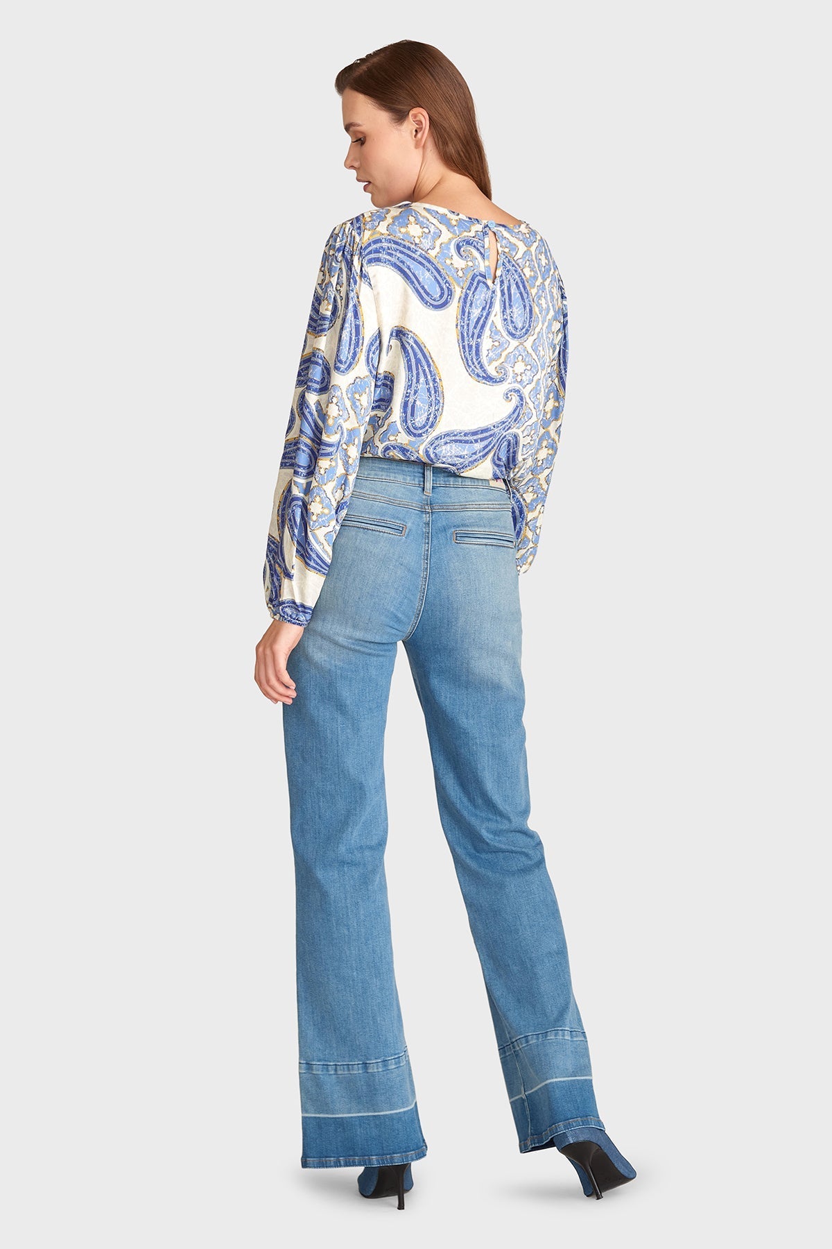 Frau in blauer Jeans und gemusterter Bluse, Rückansicht. Modetrend 2023, lässiger Look, Damenmode, stilvolle Freizeitkleidung.