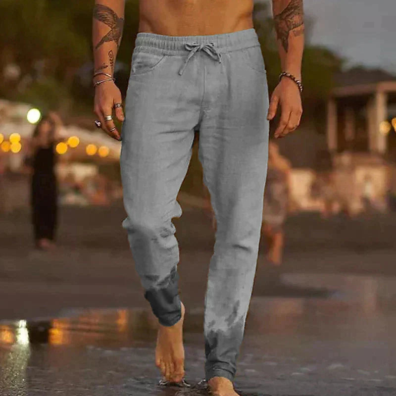 Mann in grauer Jogginghose geht barfuß am Strand entlang, Abendstimmung, Freizeitkleidung, Sommermode, entspannte Atmosphäre.