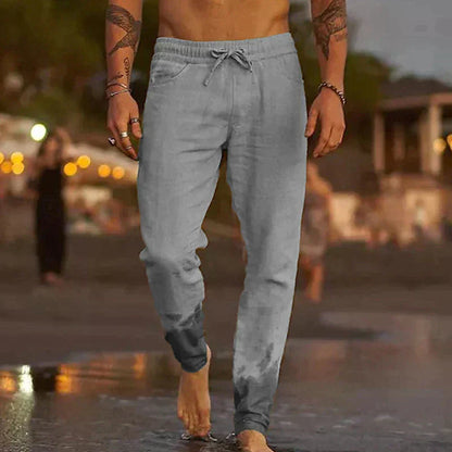 Mann in grauer Jogginghose geht barfuß am Strand entlang, Abendstimmung, Freizeitkleidung, Sommermode, entspannte Atmosphäre.