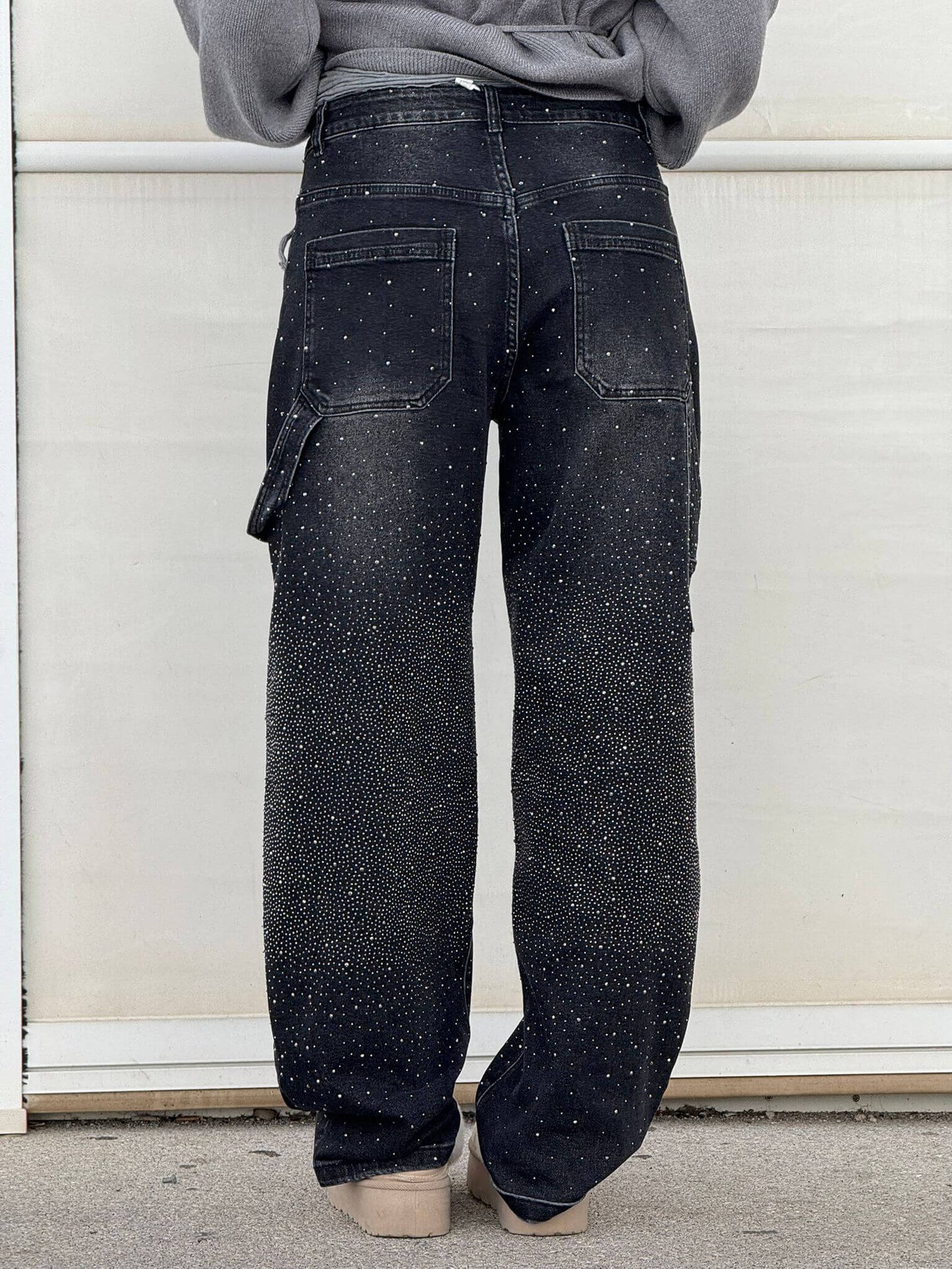 Rückansicht einer Person in schwarzen, mit weißen Punkten besprenkelten Jeans, lässiger Stil, modische Streetwear, vor hellem Hintergrund.