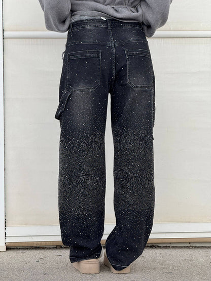 Rückansicht einer Person in schwarzen, mit weißen Punkten besprenkelten Jeans, lässiger Stil, modische Streetwear, vor hellem Hintergrund.