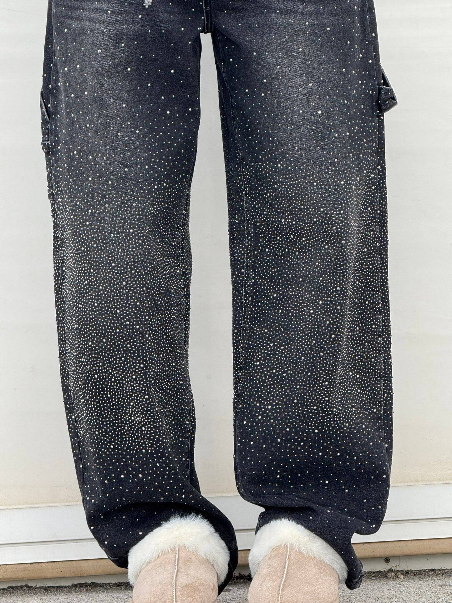 Dunkle Jeans mit funkelnden Strasssteinen, kombiniert mit beigen Stiefeln mit Fellbesatz. Modetrend, Glitzer-Jeans, Wintermode.