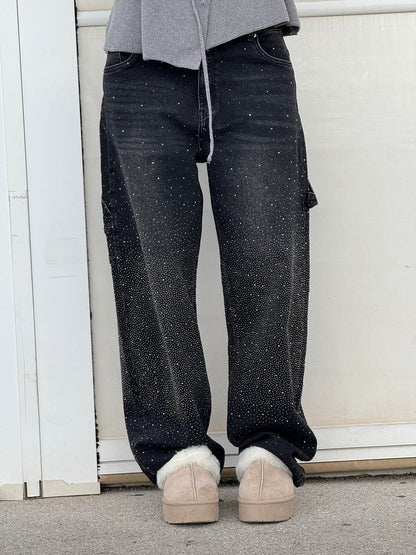 Graue Jogginghose, schwarze Jeans mit Glitzerpunkten, beige Hausschuhe. Lässiger Streetwear-Look, modisch und bequem.