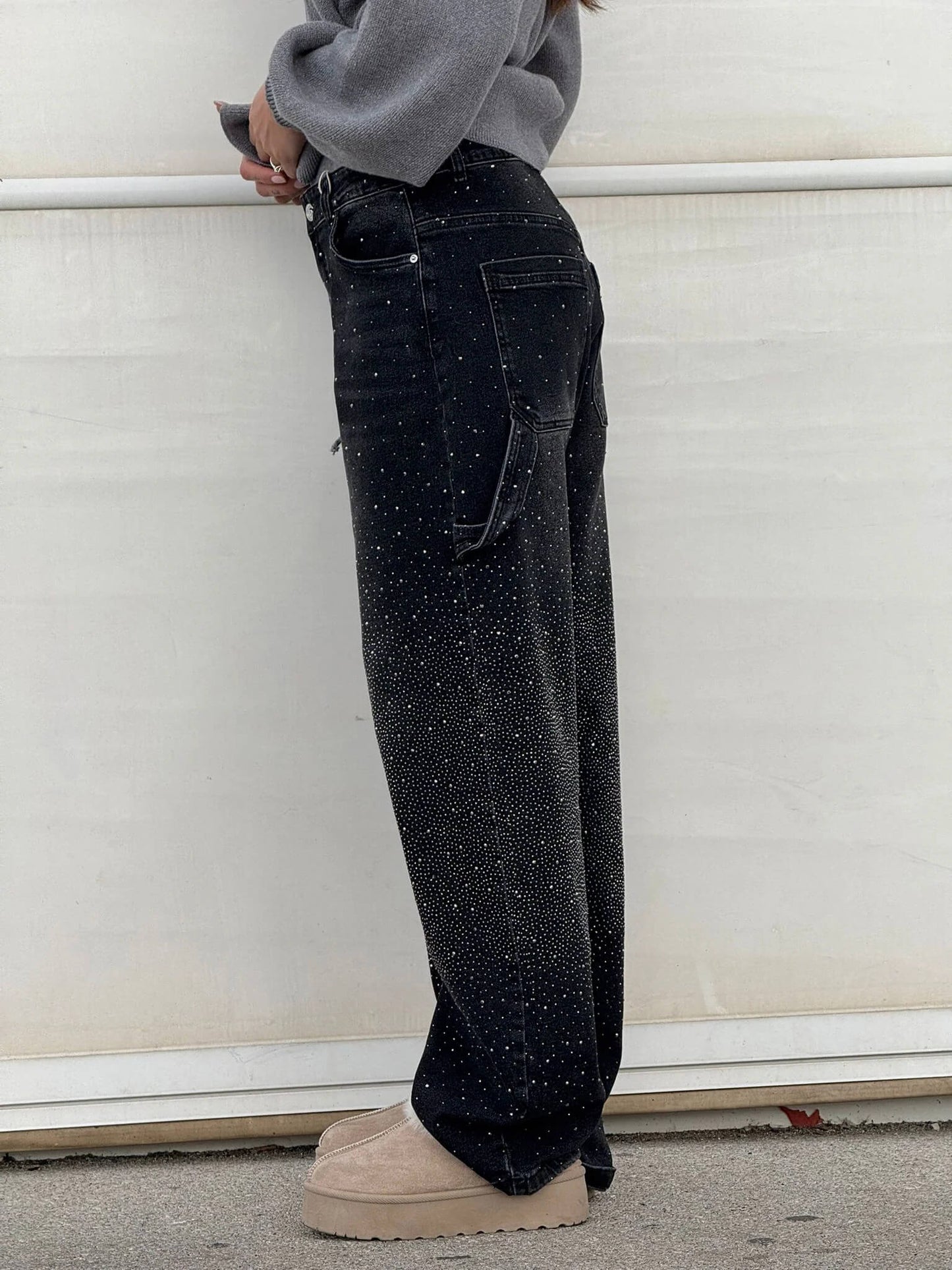 Frau in schwarzer, glitzernder Jeans und beigen Plateauschuhen vor weißem Hintergrund. Modetrend, Damenmode, Streetstyle.