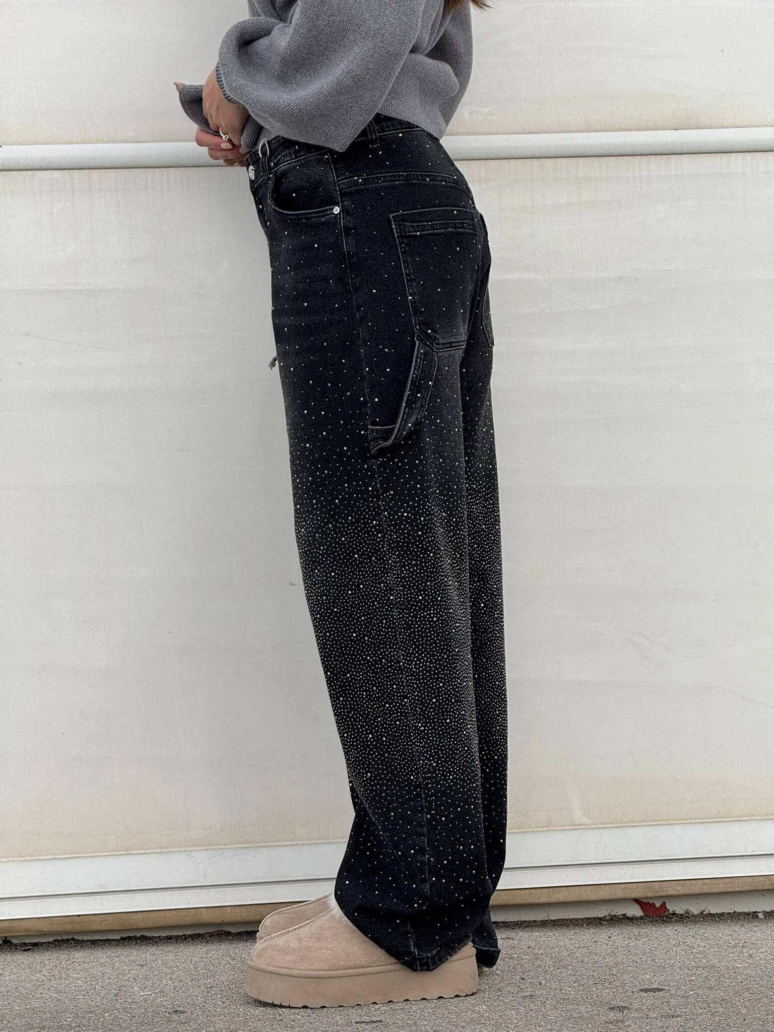 Frau in schwarzer, glitzernder Jeans und beigen Plateauschuhen vor weißem Hintergrund. Modetrend, Damenmode, Streetstyle.