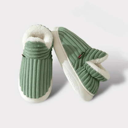 Grüne, plüschige Hausschuhe mit weißem Futter, rutschfeste Sohle, gemütlich und warm, ideal für den Winter, auf weißem Hintergrund.