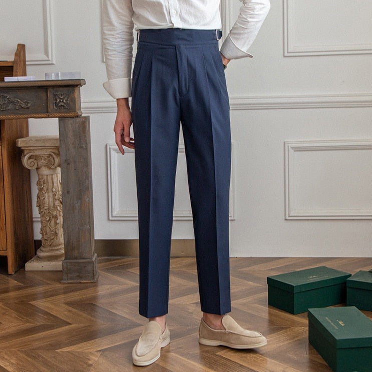 Elegante Herrenanzughose in Dunkelblau, kombiniert mit beigen Loafern und weißem Hemd, auf Parkettboden vor klassischer Wandverkleidung.
