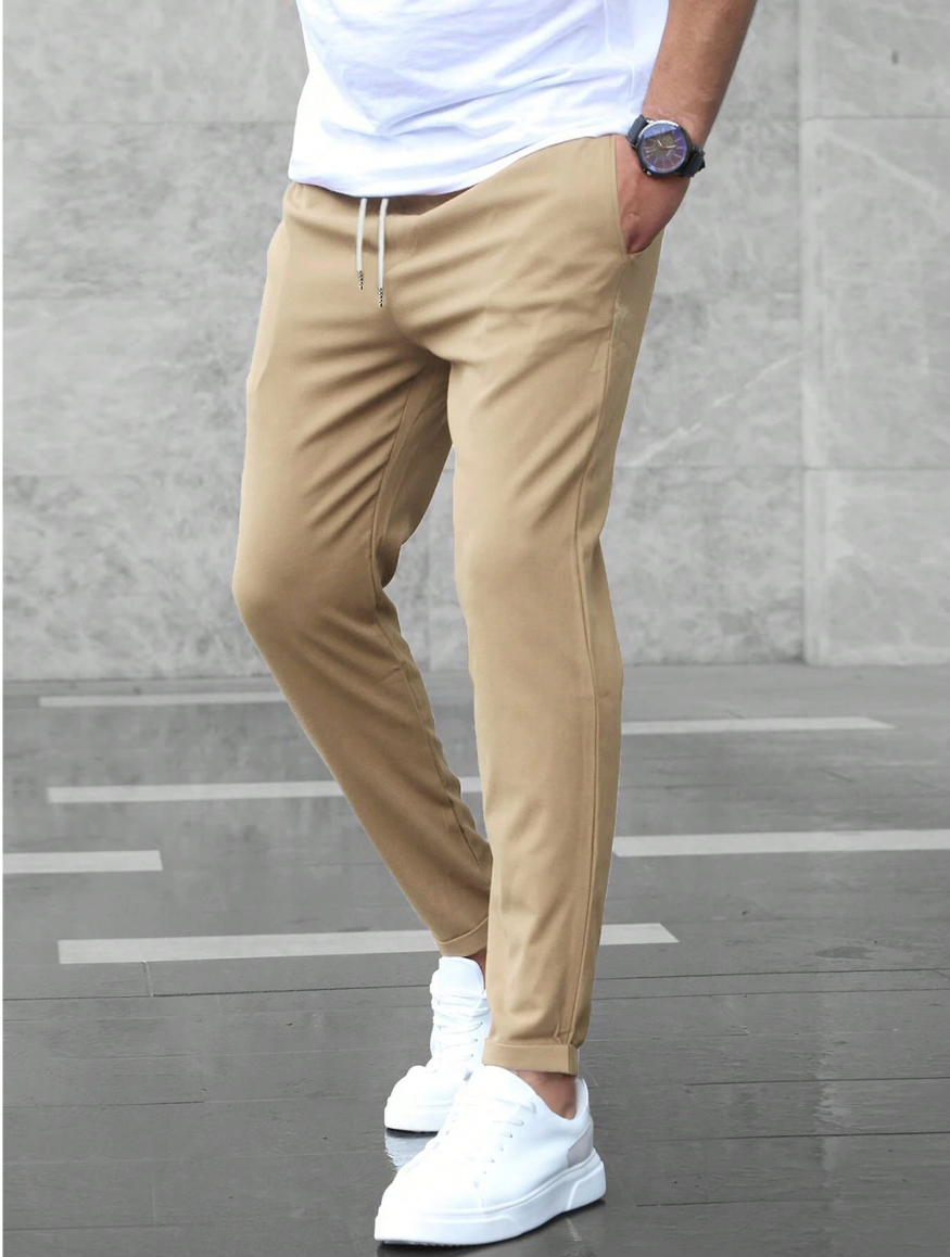 Mann trägt beige Chino-Hose und weiße Sneaker, kombiniert mit weißem T-Shirt. Moderne Herrenmode, lässiger Stil, urbane Kleidungstrends.