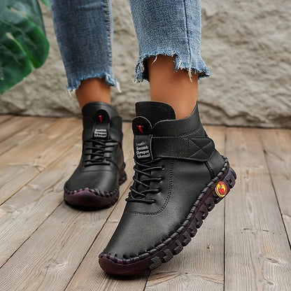 Schwarze Lederstiefel mit robuster Sohle, getragen von Person in Jeans auf Holzboden. Modische, bequeme Damenstiefel für Herbst und Winter.