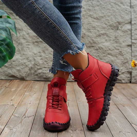 Rote Damenstiefel aus Leder mit robuster Sohle, getragen zu engen, zerrissenen Jeans auf Holzboden. Modische Herbstschuhe, Outdoor-Stil.