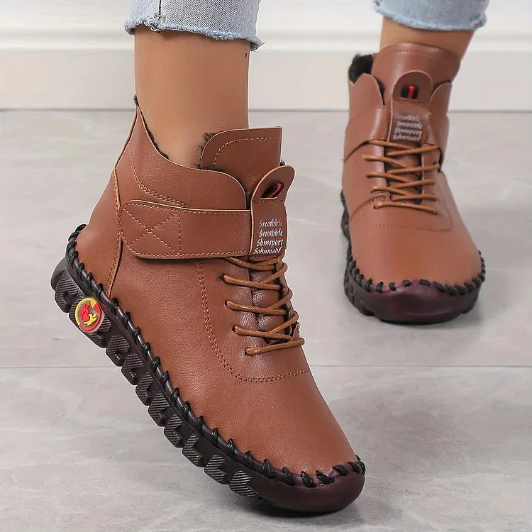 Damen-Winterstiefel aus braunem Leder mit schwarzer Sohle, Schnürung und Klettverschluss, getragen auf grauem Boden. Bequeme, warme Schuhe.