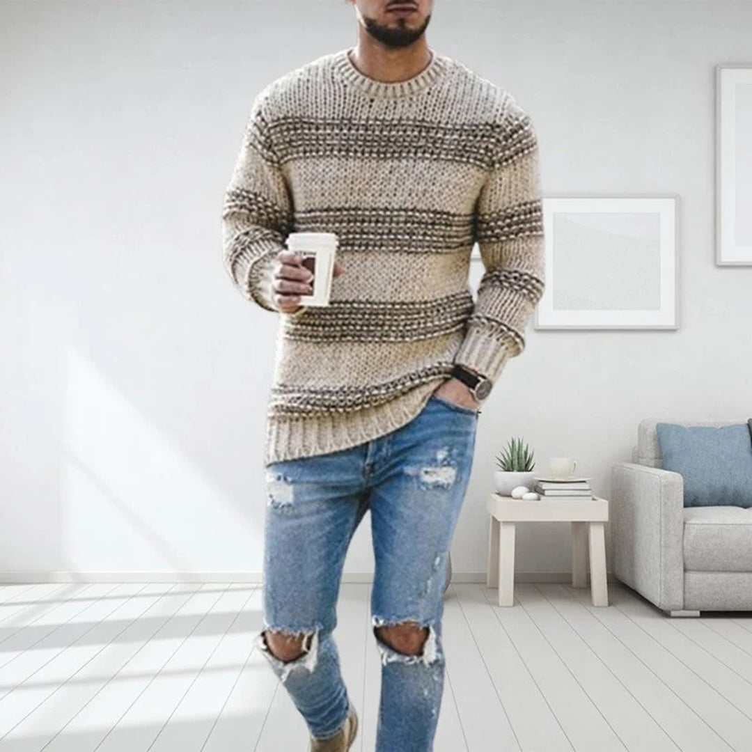 Mann in gestreiftem Strickpullover und zerrissenen Jeans hält Kaffeebecher, steht in modernem Wohnzimmer. Mode, Freizeitkleidung, Inneneinrichtung.