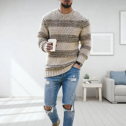 Mann in gestreiftem Strickpullover und zerrissenen Jeans hält Kaffeebecher, steht in modernem Wohnzimmer. Mode, Freizeitkleidung, Inneneinrichtung.