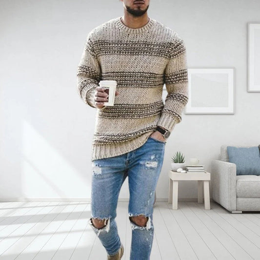Mann in gestreiftem Strickpullover und zerrissenen Jeans hält Kaffeebecher, steht in modernem Wohnzimmer. Mode, Freizeitkleidung, Inneneinrichtung.