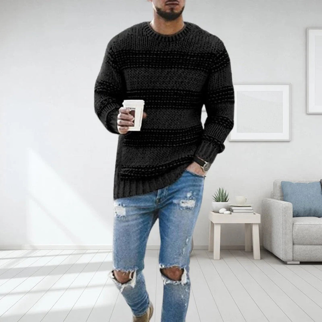Mann in modernem Wohnzimmer trägt schwarzen Strickpullover und zerrissene Jeans, hält Kaffeetasse. Stilvolle Herrenmode, lässiger Look.