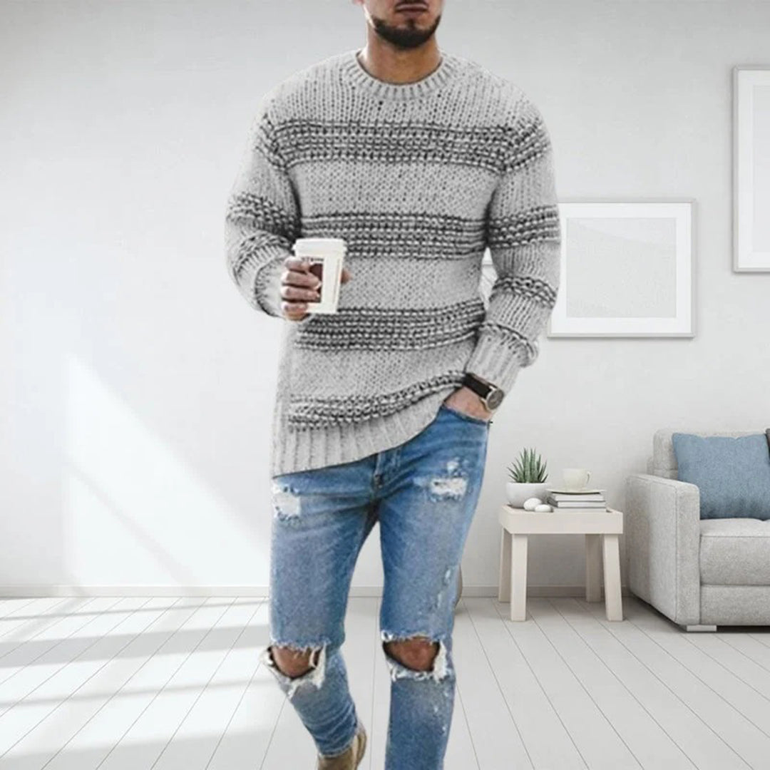 Mann in grauem Strickpullover und zerrissenen Jeans hält Kaffeetasse, steht in modernem Wohnzimmer. Mode, Freizeitkleidung, Inneneinrichtung.