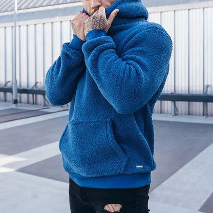 Blauer Fleece-Hoodie, getragen von tätowierter Person, urbaner Hintergrund. Modetrend, Streetwear, Herrenbekleidung, gemütlicher Stil.