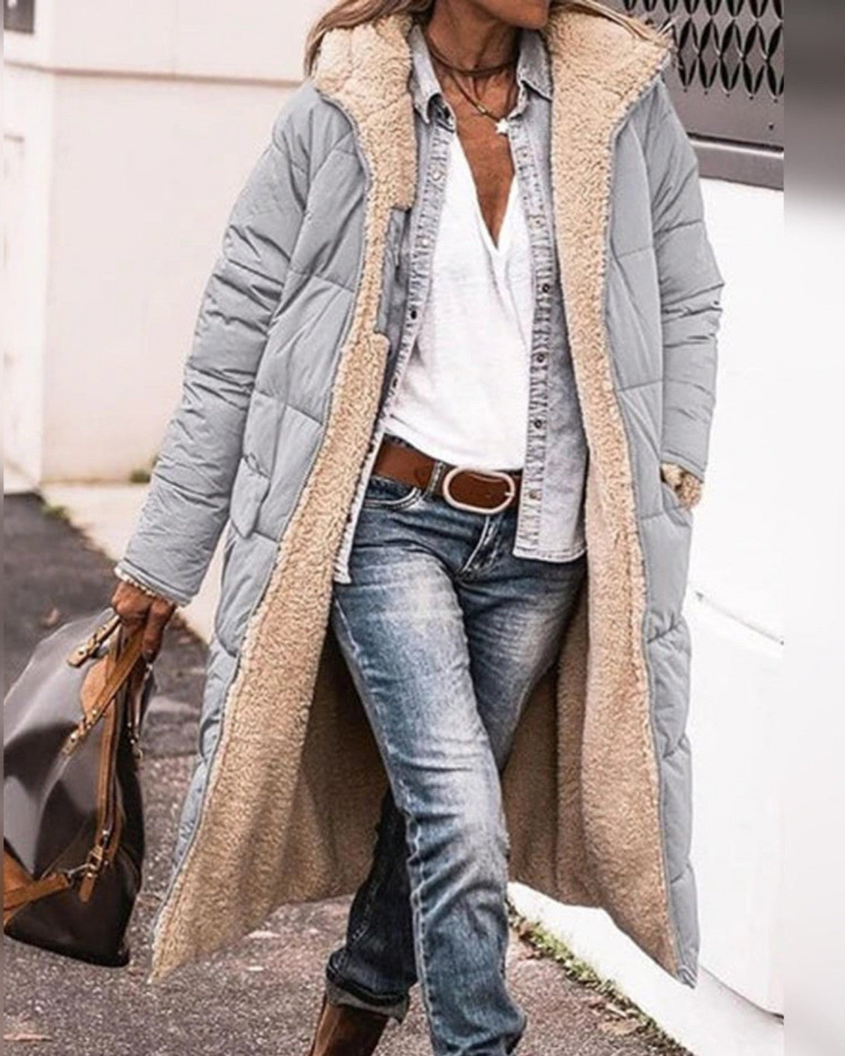 Frau in grauem, langem Steppmantel mit Teddyfutter, Jeans und weißem T-Shirt, trägt braune Tasche. Wintermode, lässiger Streetstyle.