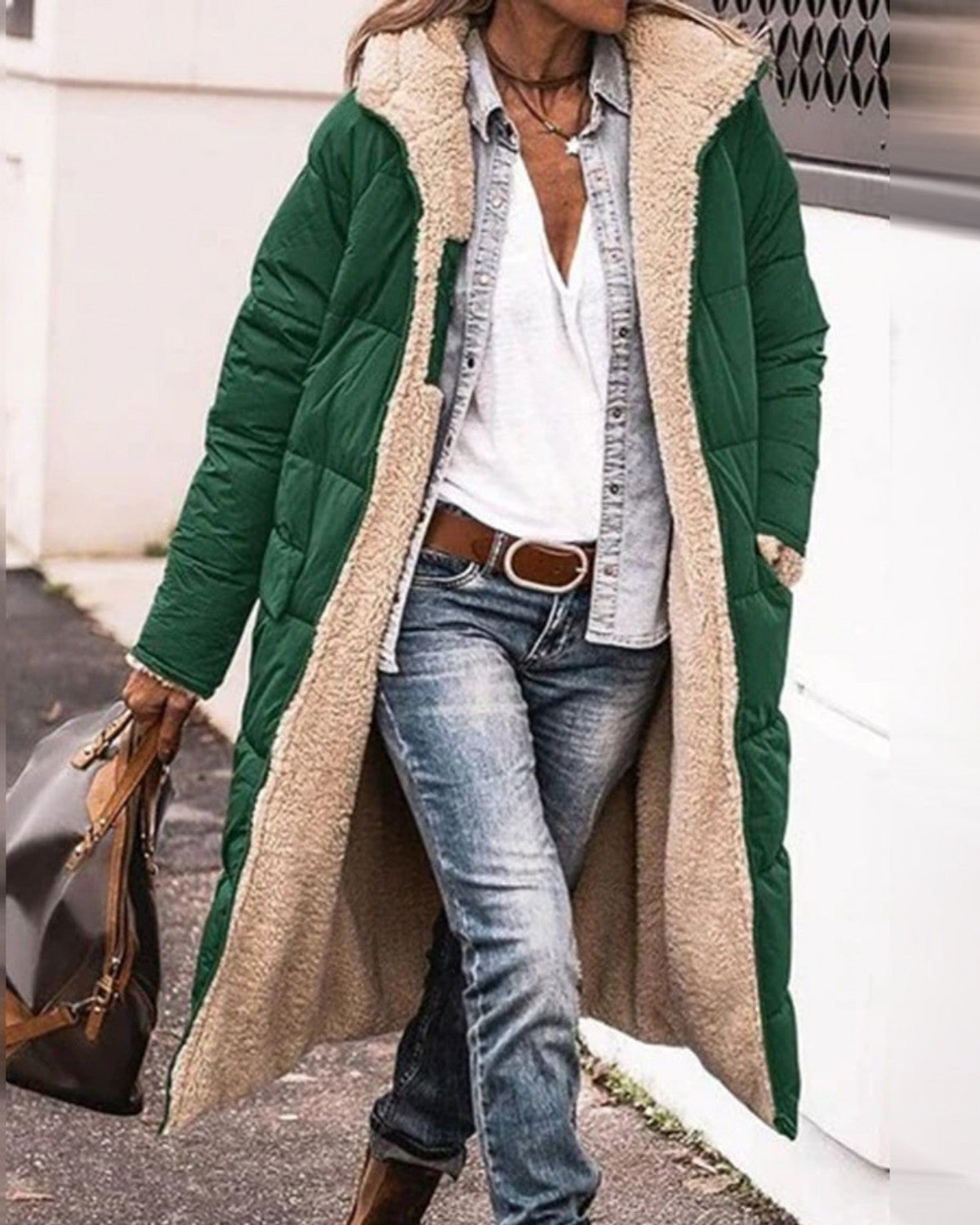 Frau in grünem, langem Wintermantel mit Fellfutter, weißem T-Shirt, Jeans und braunen Stiefeln. Modischer Herbst-Look, lässiger Stil.