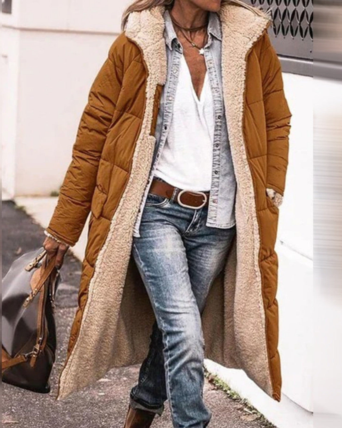 Frau in braunem, langem Wintermantel mit weißem Futter, Jeans und weißem Hemd. Modischer Herbst-Look, lässiger Stil, Outdoor-Bekleidung.