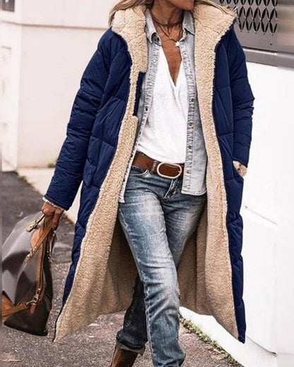 Frau in blauem, langem Steppmantel mit Fellfutter, weißem T-Shirt, Jeans und braunen Stiefeln. Modischer Winterlook, lässiger Stil.