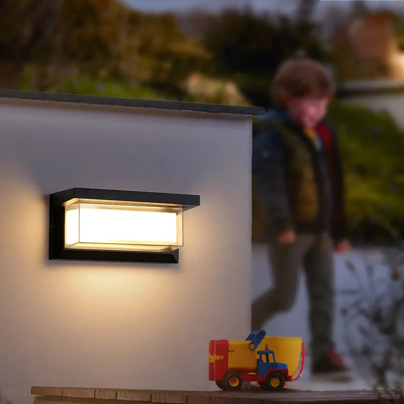 Moderne Außenwandleuchte bei Dämmerung, beleuchtet eine Mauer. Im Hintergrund unscharf ein Kind und ein Spielzeug-LKW. Ideal für Gartenbeleuchtung.