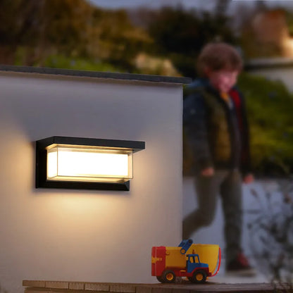 Moderne Außenwandleuchte bei Dämmerung, beleuchtet eine Mauer. Im Hintergrund unscharf ein Kind und ein Spielzeug-LKW. Ideal für Gartenbeleuchtung.