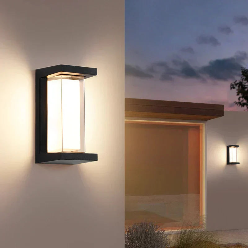 Moderne Außenwandleuchte mit rechteckigem Design, warmweißem Licht und schwarzem Rahmen, montiert an einer Hauswand bei Dämmerung.
