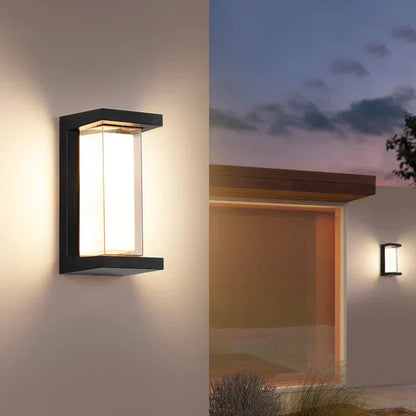 Moderne Außenwandleuchte mit rechteckigem Design, warmweißem Licht und schwarzem Rahmen, montiert an einer Hauswand bei Dämmerung.