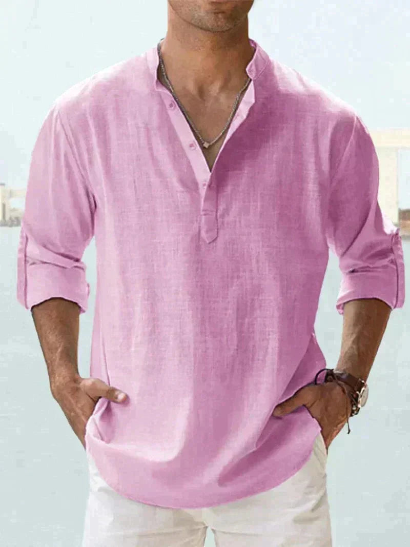 Mann in rosa Leinenhemd mit Stehkragen und Knopfleiste, lässig in die Hosentaschen greifend. Sommermode, Herrenbekleidung, Freizeitlook.