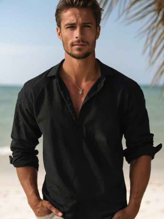 Mann am Strand in schwarzem Hemd, entspanntes Sommeroutfit, modischer Look, Meereshintergrund, lässiger Stil, Urlaubsstimmung.