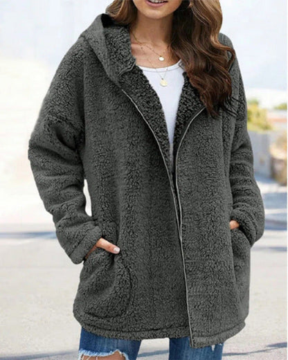 Frau in grauem Teddyfell-Mantel mit Kapuze, weißem Shirt und zerrissenen Jeans. Modetrend, Winterjacke, gemütlicher Look, Outdoor-Bekleidung.